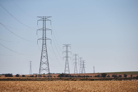 Fields with double circuit electricity transmission towers and lines in row continuing into the distance