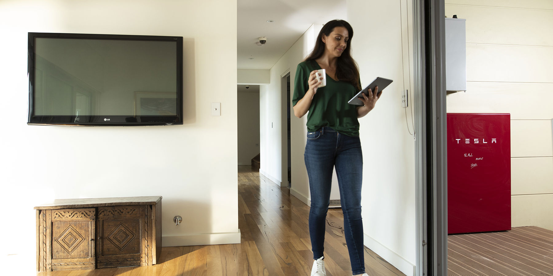 Lady stood in her house holding an iPad with a home battery visible in the background